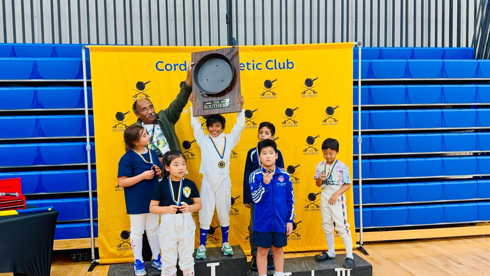 Ryan Islam holding the Southern RYC trophy above the Y8 Mixed Épée podium